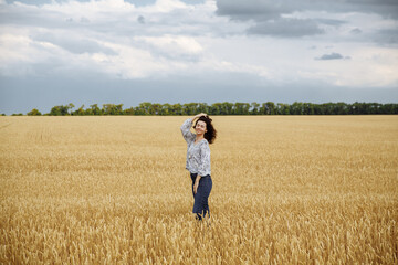 Naklejka na ściany i meble A girl in a field of yellow wheat on the background of a rainy sky