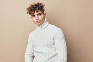 a close horizontal photo of a handsome, attractive man standing in a white knitted sweater on a beige background looking at the camera