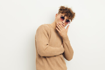 horizontal photo of a handsome, handsome man standing on a light background in beige clothes with round sunglasses holding his hand near his face