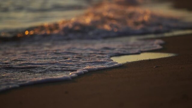 Sea waves rolling in slow-motion on empty sandy beach at sunset