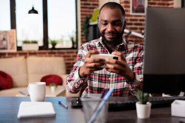 Young adult playing video games on mobile phone, having fun with online gaming competition and working from home. Enjoying game play on smartphone, freelaner doing leisure activity.