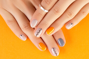Close up womans hands with trendy minimal manicure on orange background. Autumn nail design