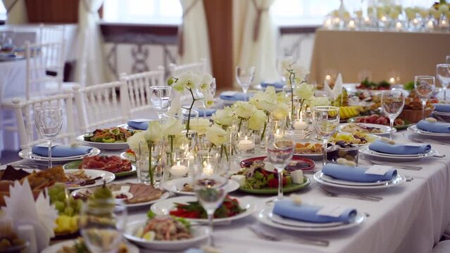 Wedding rustic style decor with dishes, drinks and roses in white and blue colours on table setting at restaurant. Banquet hall interior floristic details with flowers in glass vases filled with water