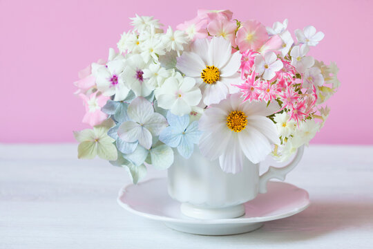 Colorful bouquet with hydrangea, cosmos flower, phlox in a cup on a white table on a pink background. Greeting card for the holiday.