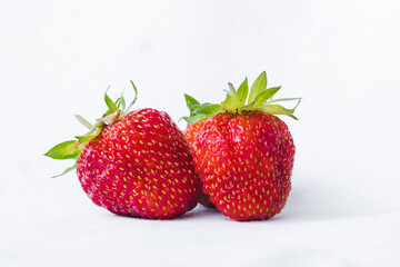 Three ripe strawberries with strawberry leaf, isolated on a white fabric background. Bunch of strawberries. Healthy eating and harvesting farm organic food concept