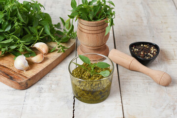 Homemade fresh herbal  Italian pesto sauce, green basil leaves, pine nuts, garlic, black pepper and olive oil served in glass bowl on wooden background
