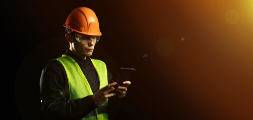 Engineering consulting, a male builder in a hard hat on a dark background uses a tablet. Business...
