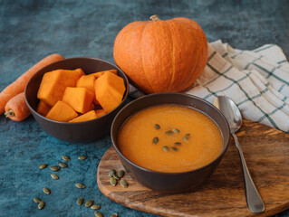 Pumpkin cream soup in a bowl with a spoon on wooden board on the table next to pumpkin whole and cut into pieces.  Healthy, vegetarian food. Diet. Home cooking. Thanksgiving day. Halloween.