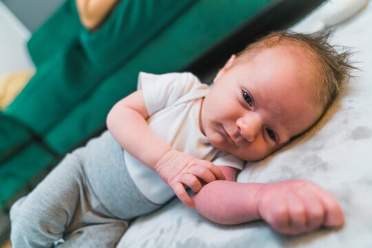 White newborn baby boy in comfy clothes laying on the floor on his side looking into camera with pleasant expression. Horizontal indoor shot. High quality photo