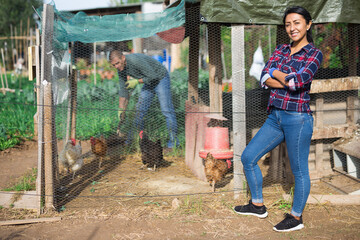 Latina woman farmer in checked shirt feeding chickens at farm