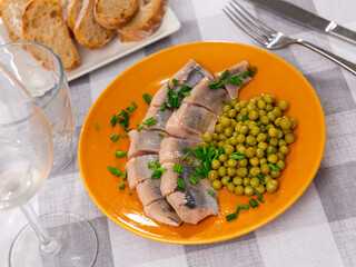 Appetizing sliced herring with canned green peas, decorated with fresh green onions on top