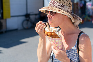 Attractive woman wearing sunglasses and straw hat, in a light summer dress, eating ice cream off a...