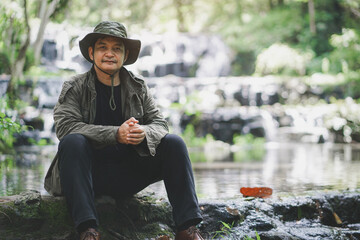Asian traveler in a hat sits in the waterfall area relaxing and happy