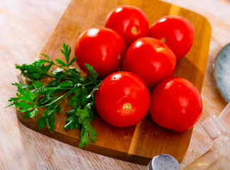 Delicious ripe tomatoes with fresh parsley, lying on a wooden surface. Ingredients for cooking