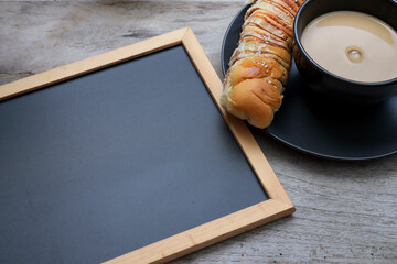 Empty black chalkboard on the wooden table with a loaf of red bean bread and a cup of coffee