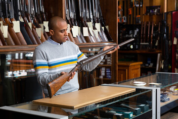 Portrait of focused male standing with rare collectible rifle in hunting shop indoors