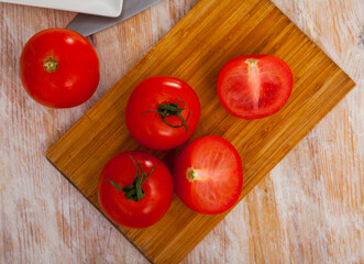 Ripe juicy tomatoes on cutting board on kitchen table. Preparing food concept.