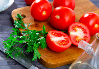 Ripe tomatoes with fresh parsley lying on a wooden chopping board during cooking. Close-up image