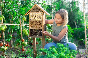 Portrait of happy girl next to hotel for insects in of wooden birdhouse in the garden - obrazy, fototapety, plakaty