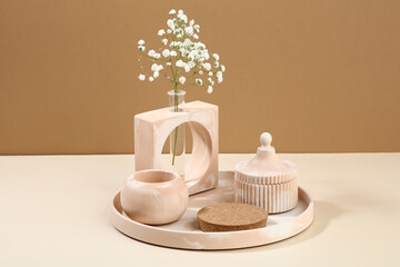 Modern DIY concrete home decor on beige background. Vase of flowers, cup, podium for cosmetics product presentation.