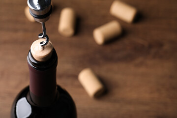 Opening wine bottle with corkscrew on wooden table, closeup. Space for text