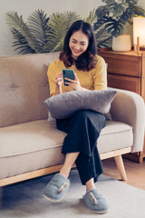 Obraz premium Young Asian woman relax on cozy sofa furniture in living room using browsing Internet on tablet, Asian girl lying resting on comfortable couch at home watching movie or video on pad.