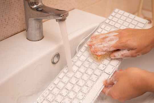 Woman washing white computer keyboard with a sponge with foam.