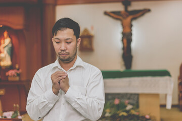 Obraz premium Asian man praying in a Christian church. man praying on holy bible in the morning. asian mand hand with Bible praying,Hands folded in prayer on a Holy Bible in church concept for faith, spiritualit