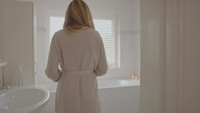 Beautiful woman walking towards filled bathtub and opening her robe