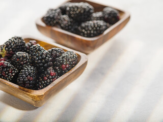 On a white background, two wooden bowls with ripe blackberries. Light dessert, vitamins, antioxidants, sweet vegetarian and diet food, ingredient for confectionery, sauces.