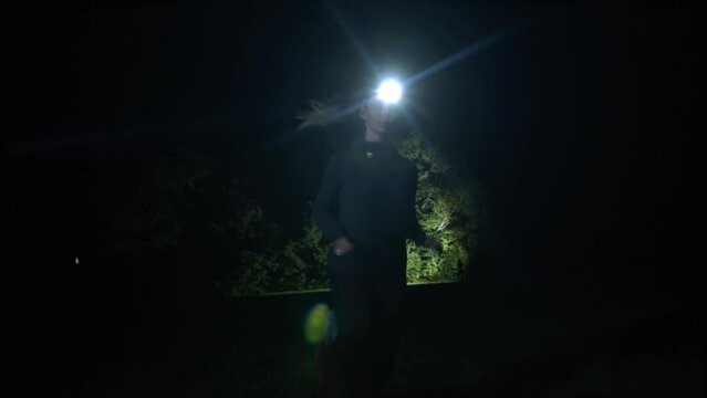 A woman runs in the middle of nature with her headlamp at night