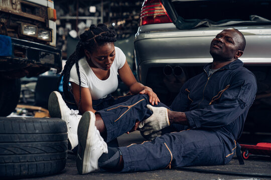 Woman auto mechanic giving first aid to man auto mechanic suffering after working injury in car repair shop, Injury at work. 