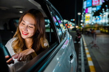 Happy beautiful woman texting smartphone sitting car back seat in urban, Asian businesswoman working late commuting from office in Taxi backseat with mobile phone in city at night after late work