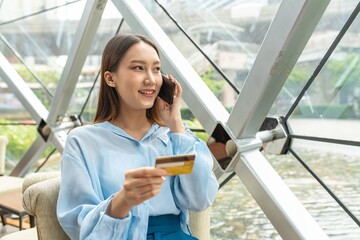 Young beautiful asian female businesswoman lady calling the bank credit card center to ask for credit line increase to make a online payment purchase while in a random cafe