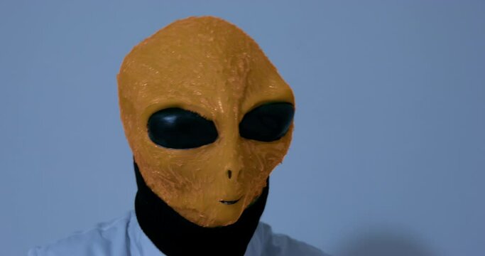 Alien looks around and does strange movements shaking head in room. Extraterrestrial person stands against white wall suddenly disappearing closeup