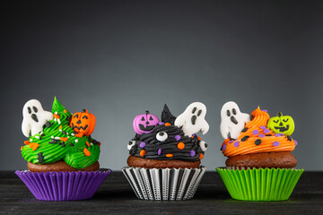 Cupcake on Halloween. Pumpkin Jack o lantern and ghost. Dessert on Halloween party. Muffin decorated with colored sprinkles, frosting and Icing. Dark background with copy space. High quality photo