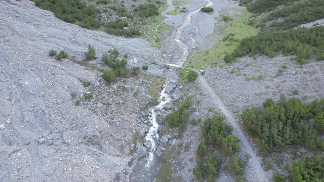 Aerial drone footage flying along a river and slowly tilting to reveal a dramatic glacial valley surrounded by a steep mountains and pine trees with patches of snow in Switzerland.
