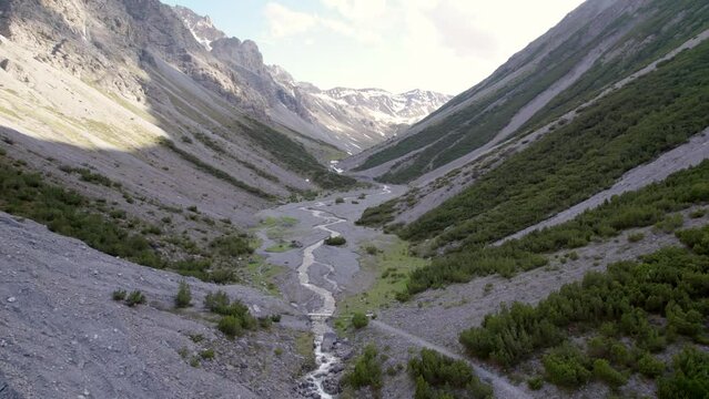 Aerial drone footage reversing upwards through a dramatic glacial valley surrounded by a steep mountains and pine trees with patches of snow and an alpine river in Switzerland.