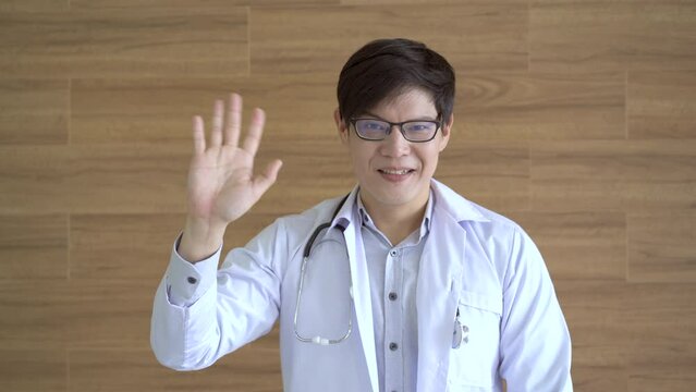 Asian doctor smiling to camera and waving hand.