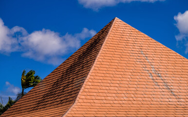 High Peaked Orange Roof with Blue Sky and Cumulus Clouds Above.