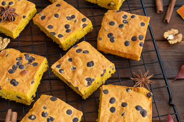 Pumpkin blondie or cake with chocolate drops, walnuts, cinnamon and anise on a dark wooden background. Dessert for Thanksgiving or Halloween.
