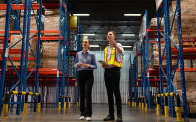 Obraz premium Warehouse manager talking and pointing towards shelf while checking product in warehouse, Logistic industry concept.