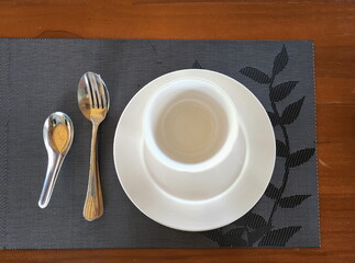 Round plates and white ceramic serving cups are stacked on black plates with leaf and twig motifs. By placing the stainless steel cutlery on the left side with the middle spoon.

