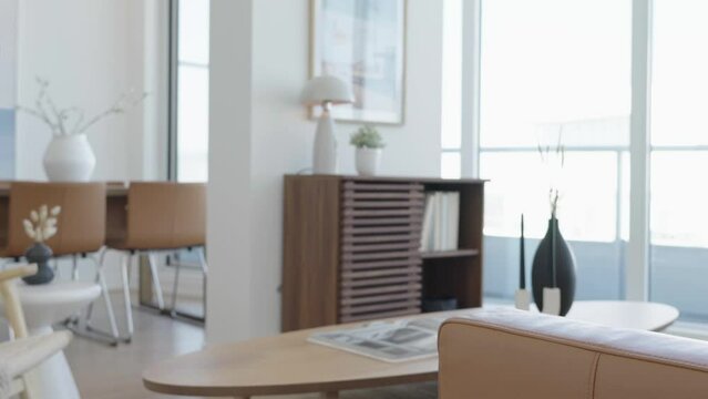Knee level rising shot of the living area in a high ceiling penthouse condominium unit focus from sofa armrest to storage shelf at the back during a sunny day