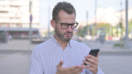 Upset Young Adult Man Reacting to Loss on Smartphone Outdoor