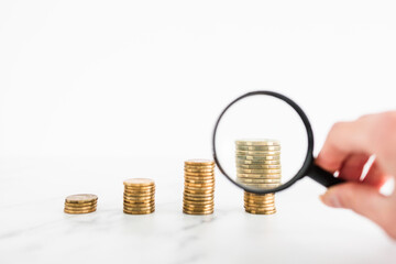 growing stacks of coins with magnifying glass analysing them, increasingly expensive prices or...