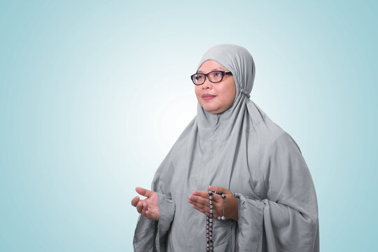 Portrait of Asian woman wearing prayer gown or mukena while praying with hands raised. Isolated image on white background