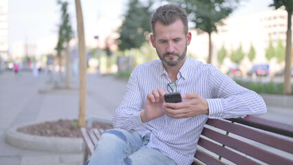 Young Adult Man Using Smartphone while Relaxing on Bench