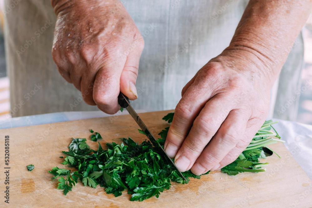 Wall mural Female hands cuts fresh herbs for salad, soup or sauce preparation. Organic food, vegetarianism