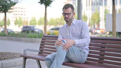 Fototapeta premium Young Adult Man having Knee Pain while Sitting on Bench Outdoor